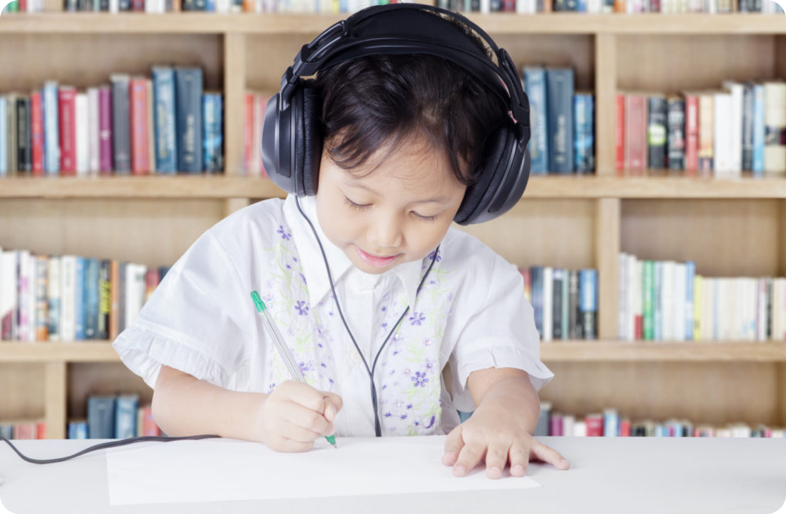 Ein Kleinkind mit Kopfhörern zeichnet auf Papier. Im Hintergrund ist ein Bücherregal zu sehen.