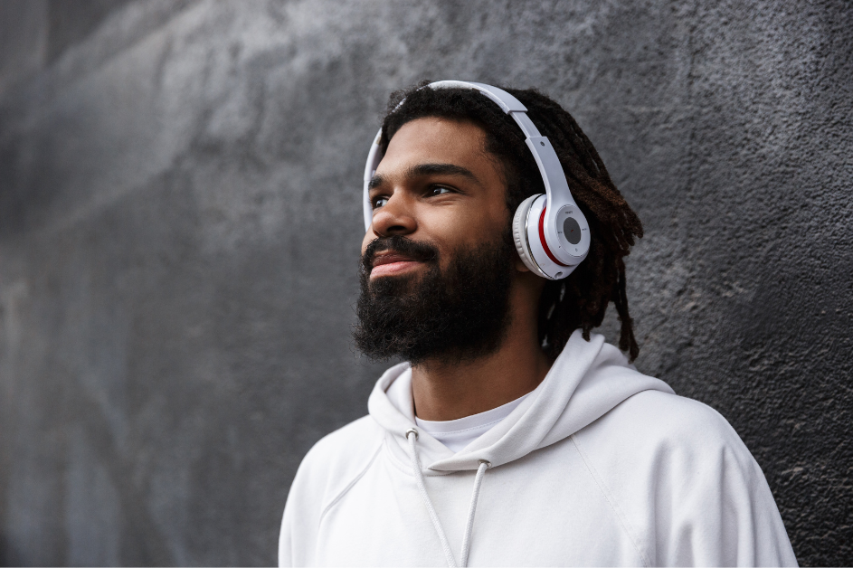 Young man with headphones smiling against a textured gray wall, wearing a white hoodie.