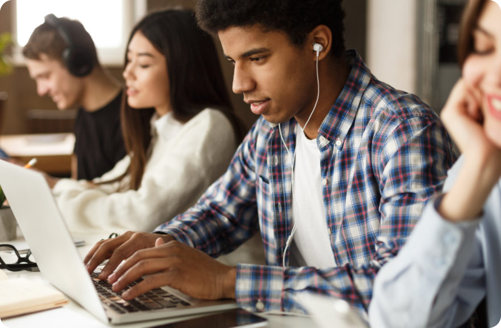 Diverse Schülerinnen und Schüler lernen mit Laptops und Kopfhörern gemeinsam in einem hellen Raum.