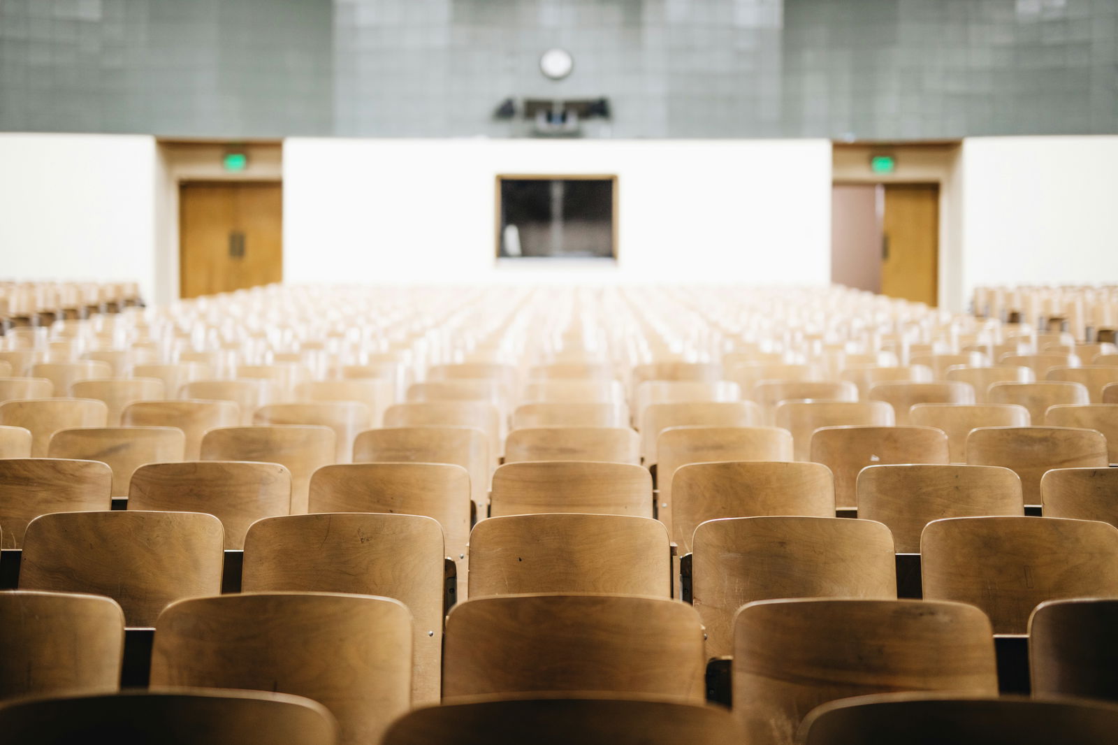 Interior of an empty auditorium with rows of wooden chairs and a simple stage backdrop.