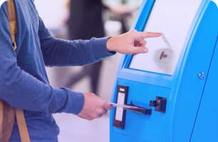Person using a blue self-service kiosk, inserting a card for transaction assistance.