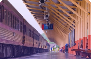 Train station platform with colorful benches, digital display, and two trains parked nearby.