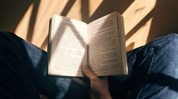 A person sitting on a chair, engrossed in an open book, captivated by the words on its pages.