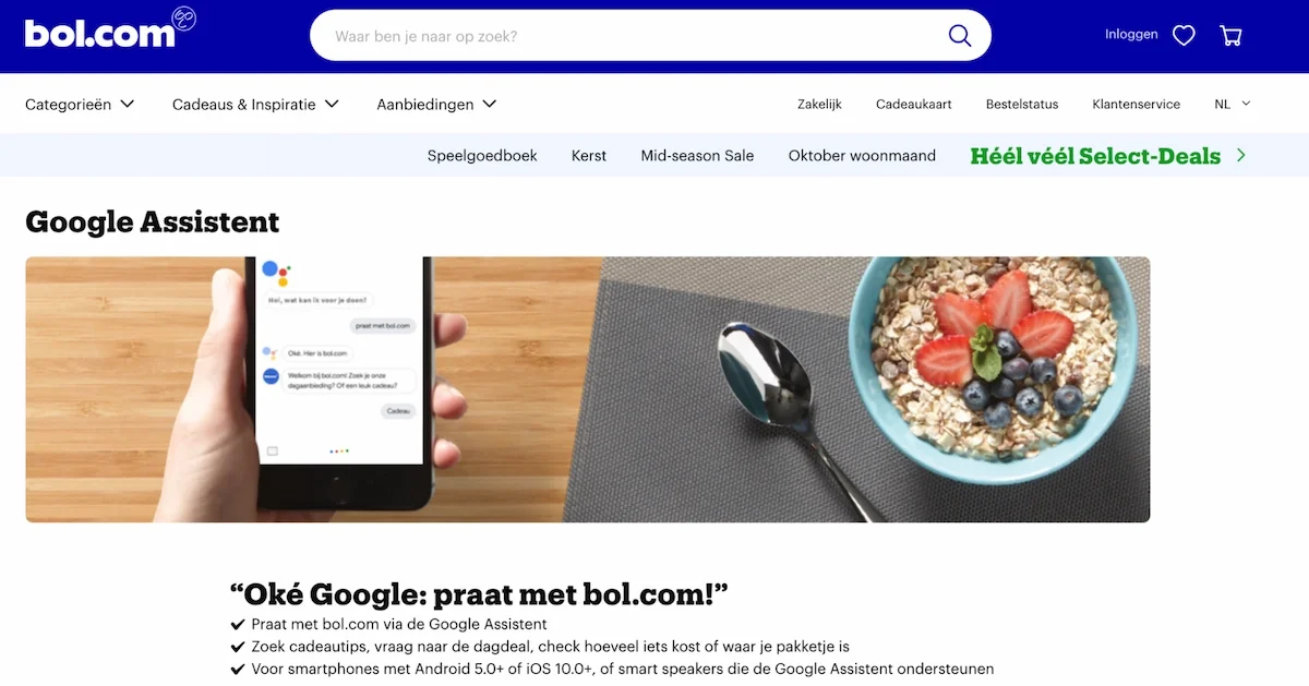 Screenshot of the web page on the bol.com website about Google Assistant. The image shows a bowl of cereals and a hand holding a smartphone being used to communicate with bol.com using Google Assistant. The text under the image is in Dutch and translates to: Okay, Google, talk to bol.com! Look for gift tips, the deal of the day, what something costs, or where your package is. Works for smartphones with Android 5.0 or higher, iOS 10.0 or higher, and also for smart speakers that support Google Assistant.