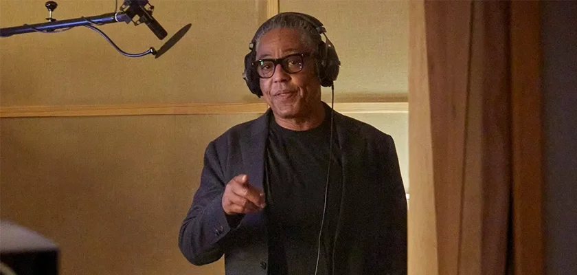 Actor Giancarlo Esposito, known for roles in Breaking Bad and The Mandalorian, stands in a recording studio wearing headphones and pointing towards the listener. A microphone is visible to his left.