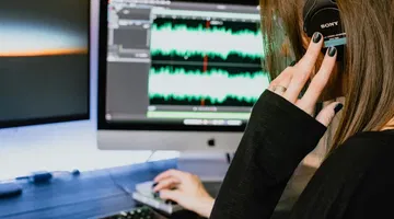 Eine Frau hört über Kopfhörer am Computer zu.