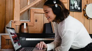 A woman wearing headphones uses a laptop to decide on assistive technology: ReadSpeaker Text to Speech, free TTS, or both?