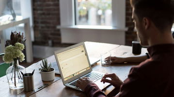 Man operating laptop on top of table.