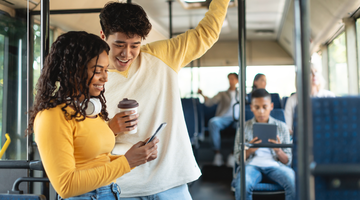 A man and a woman on the bus look at a smartphone and smile.