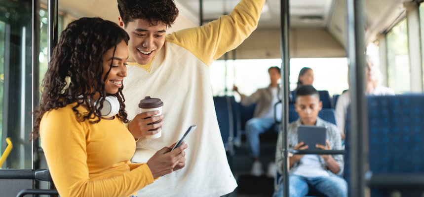 A man and a woman on the bus look at a smartphone and smile.