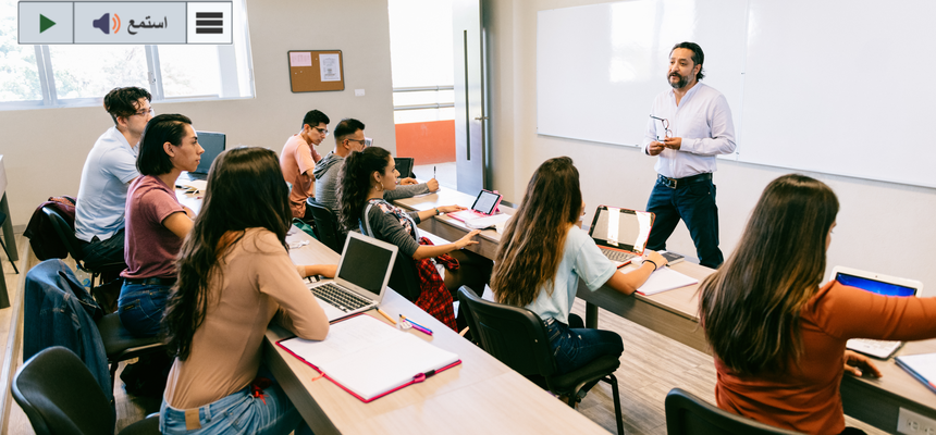 Students in a classroom listen to the teacher standing at the board.