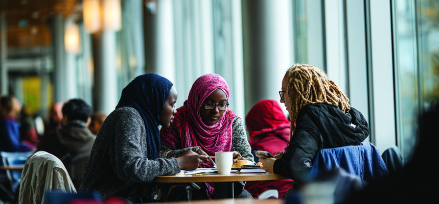 Three women learn around a table in a library.