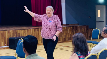 A woman standing on stage in front of an audience, giving a presentation.