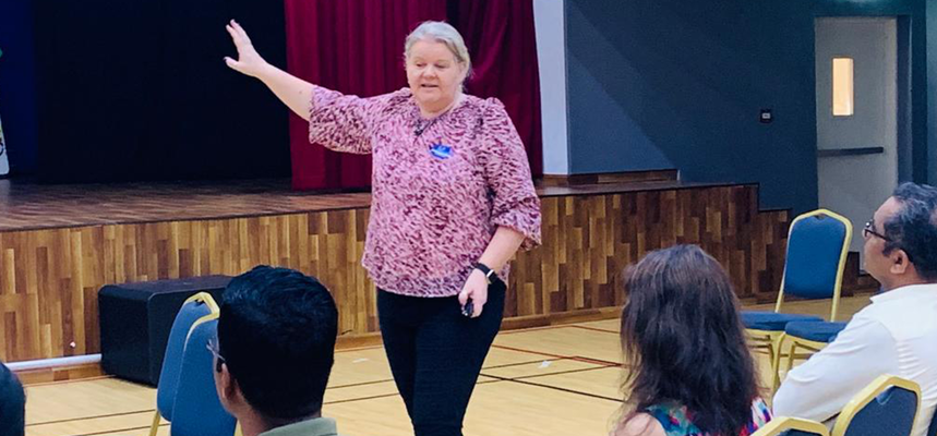 A woman standing on stage in front of an audience, giving a presentation.