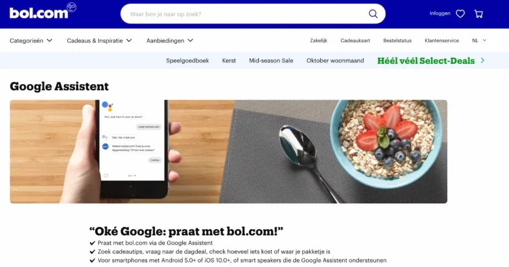 Skærmbillede af siden om Google Assistant på bol.com’s hjemmeside. Billedet viser en skål korn og en hånd, der holder en smartphone, der bruges til at kommunikere med bol.com ved hjælp af Google Assistant. Teksten under billedet er på hollandsk og betyder oversat: Okay, Google, tal med bol.com! Find gavetips, dagens tilbud, hvad ting koster, eller hvor din pakke er. Virker til smartphones med Android 5.0 eller nyere, iOS 10.0 eller nyere og også til smarthøjtalere, der understøtter Google Assistant.