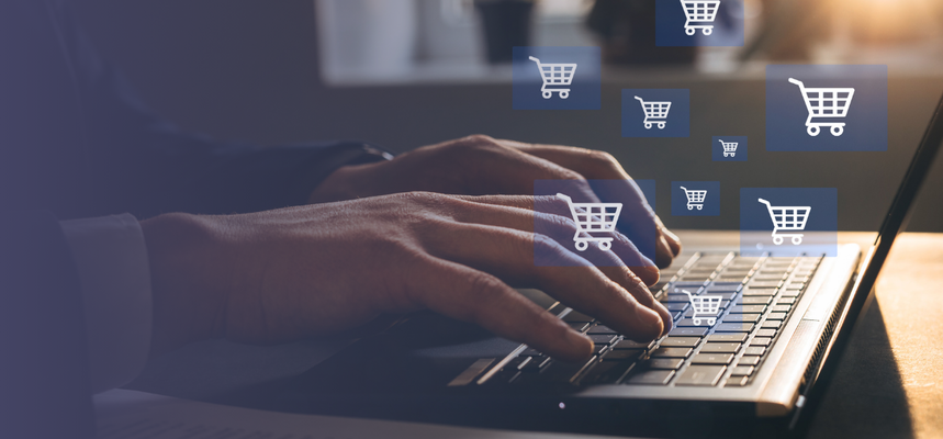 A person is typing on their laptop with shopping cart icons floating above the keyboard.
