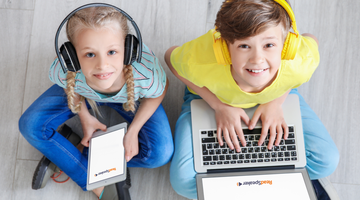 Two children are using computers while smiling.