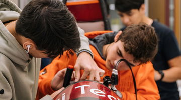 Two male apprentices working side by side, on race car mechanics.