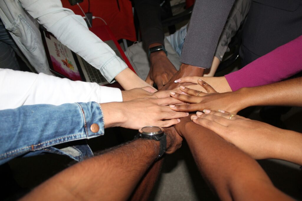 Group of people standing in a circle with their hands joining in the middle, representing equity and success.