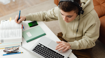 Étudiant assis à un bureau utilisant un ordinateur portable et un casque pour un apprentissage accessible..