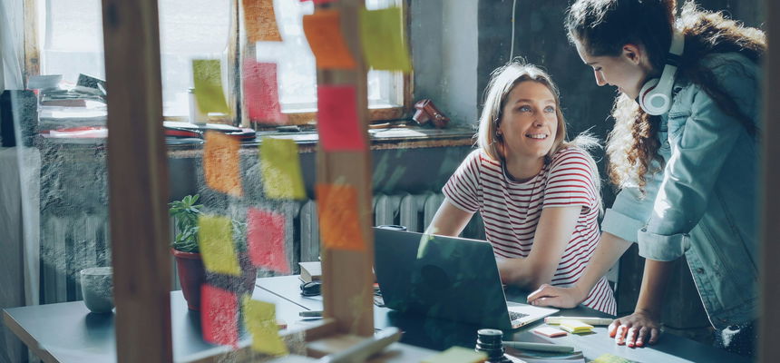 Two women working around a computer in a work environment.