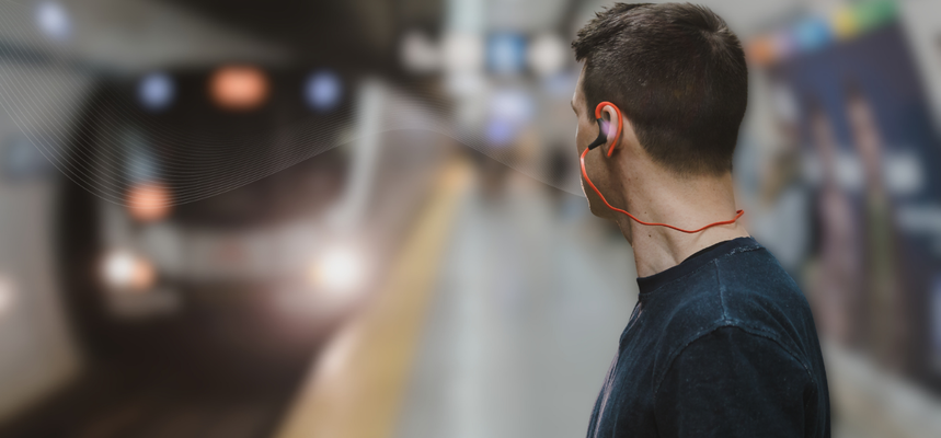 A wide horizontal banner featuring a man from the side, seen from the chest up, standing on a blurred subway platform as a train approaches in the background. He is wearing a dark t-shirt and bright orange wired earbuds. A subtle, white flowing wave sound line pattern emanates from his ear conveying a transport announcement, moving toward the left side of the frame across the subway station setting.