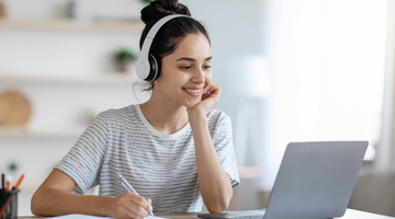 Image of a student sitting at a desk with a computer wearing headphones actively participating in audio as part of digital learning.