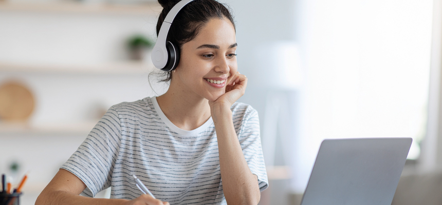 Image of a student sitting at a desk with a computer wearing headphones actively participating in audio as part of digital learning.