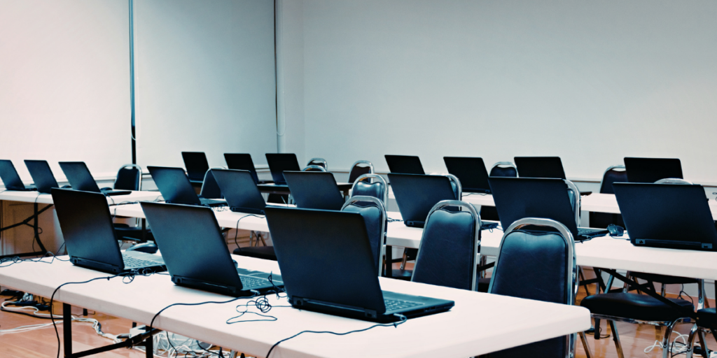 Image of classroom with multiple laptops lined up across three lines of desks to represent digital assessments.