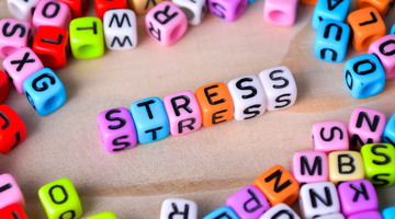 A line of 6 brightly pink, blue, orange and white cube-shaped beads, with black letters on each one spelling out 'stress'.