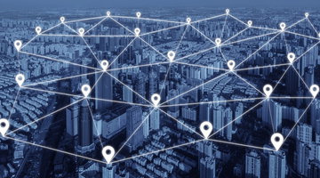 High angle birds-eye view of a vast modern city tinted deep blue, overlaid with a luminous geometric network of glowing white location pin icons connected by thin glowing white lines, forming a digital web over the entire metropolitan landscape
