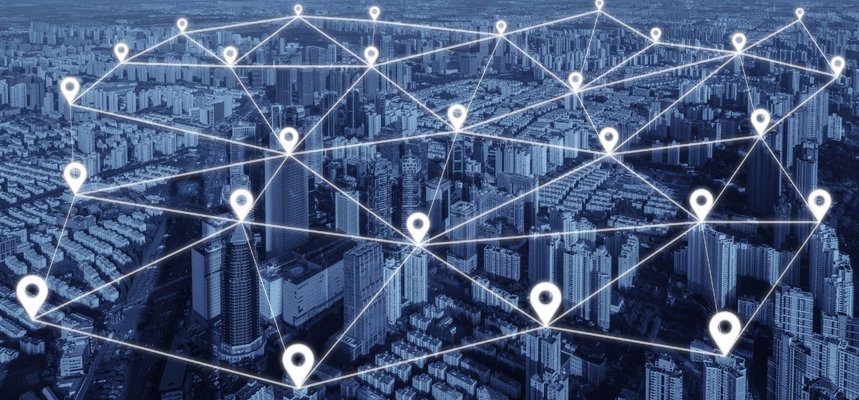 High angle birds-eye view of a vast modern city tinted deep blue, overlaid with a luminous geometric network of glowing white location pin icons connected by thin glowing white lines, forming a digital web over the entire metropolitan landscape