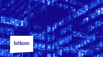 Modern multi-story office building at night with hundreds of illuminated windows, photographed in deep blue tones with the white bitkom logo panel on the facade.