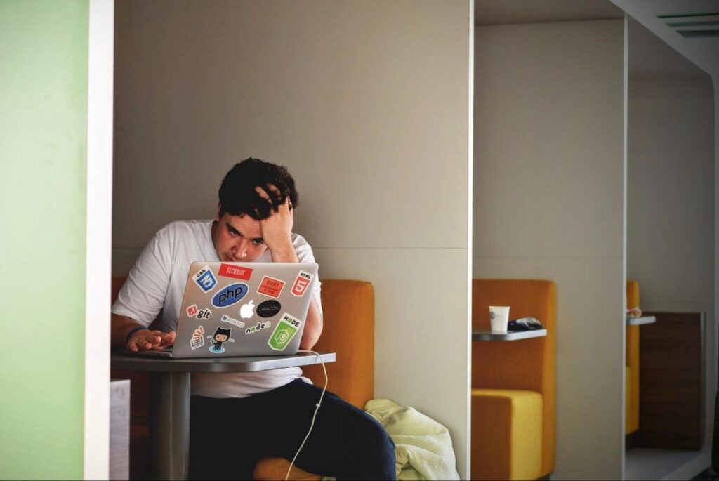A man resting his head on his hand while sitting at a table, trying to concentrate on the computer screen.