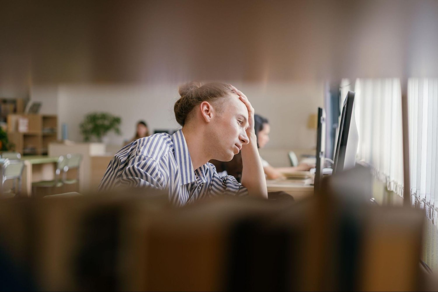 A man seated at a desk, focused on his computer screen, with a notepad and pen nearby. He looks focused, and his surroundings are blurry.