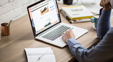 A man focused on his laptop, seated at a desk with a notepad and some books nearby.