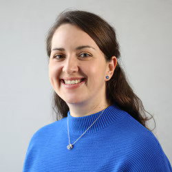 Portrait of Irene Custodio, Digital Assessment Design Lead at Pearson, smiling and wearing a bright blue ribbed jumper.