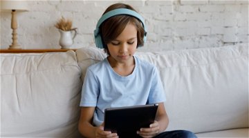 Un niño con auriculares escucha en su tableta un texto leído en voz alta