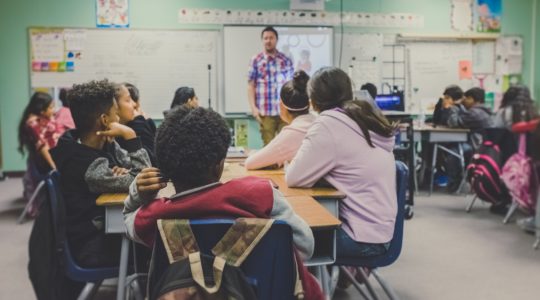 Studenten zitten in een klas en luisteren naar de leraar op het bord.